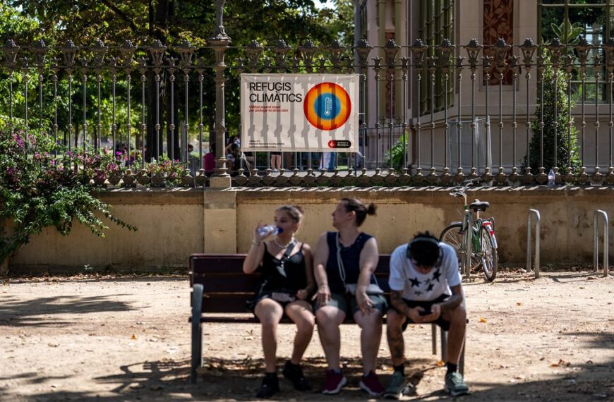 Tres persones assegudes en un banc a l'ombra a Barcelona. Beuen aigua per combatre l'onada de calor.