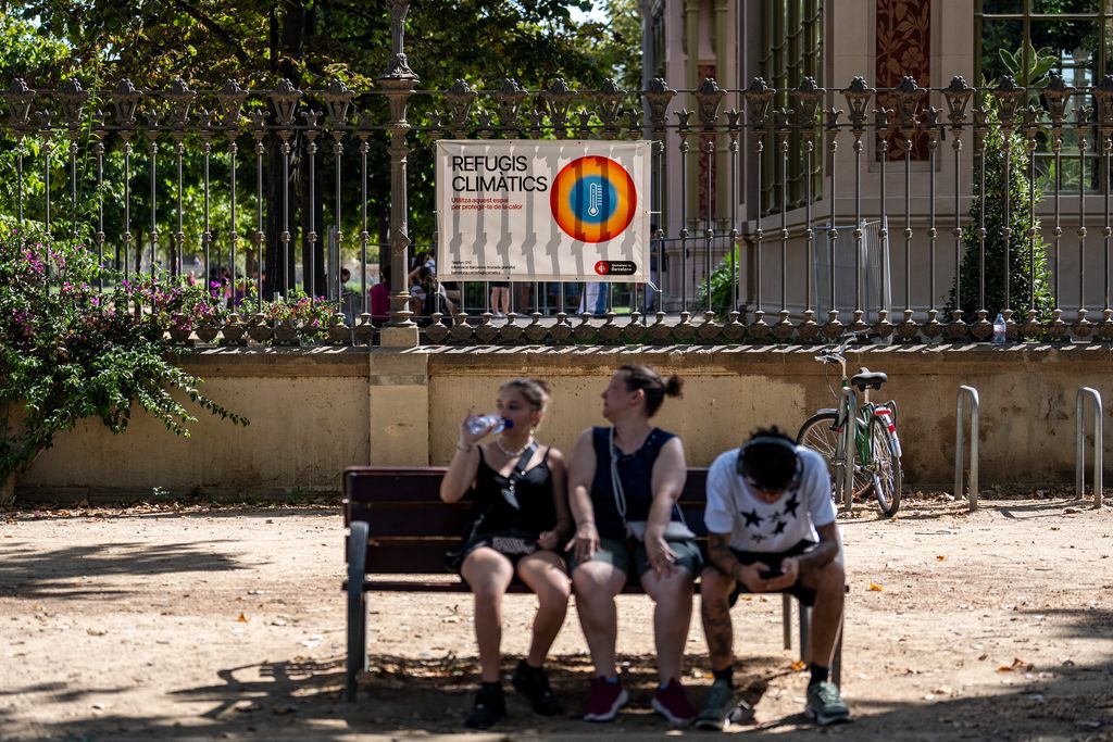 Tres persones assegudes en un banc a l'ombra a Barcelona. Beuen aigua per combatre l'onada de calor.