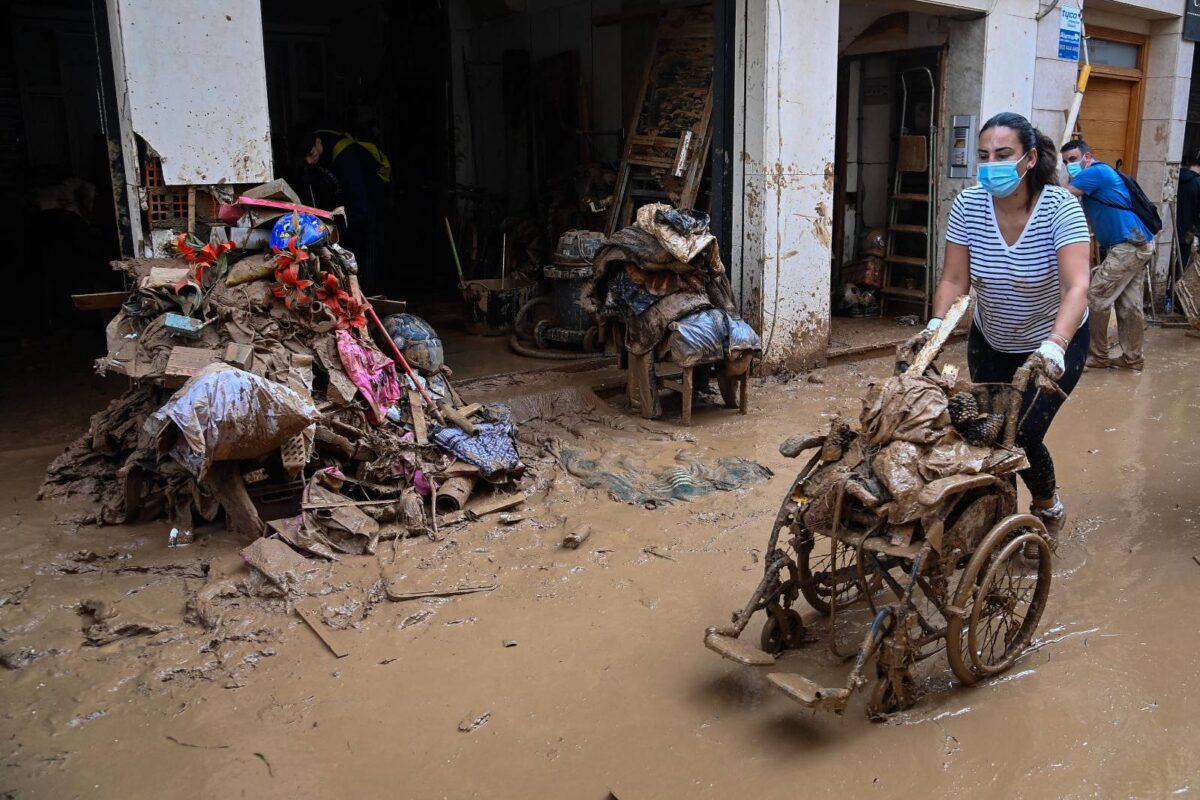 Una dona arrossega una cadira de rodes plena de brossa pel fang després de les inundacions a Paiporta, València. JOSE JORDAN / AFP