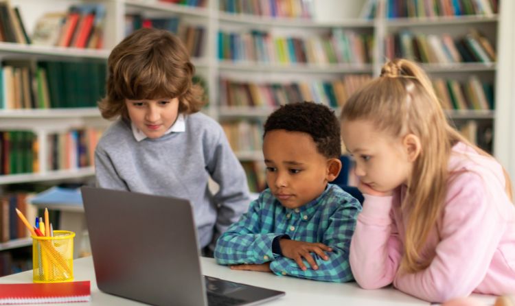 Tres nens a una biblioteca mirant una pantalla d'ordinador